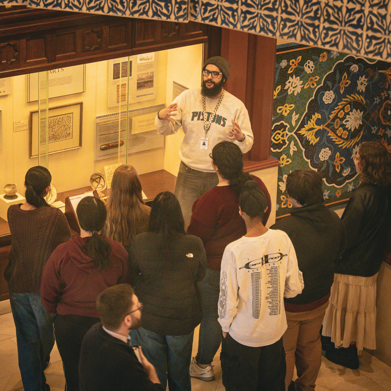 A tour guide in front of a group of students with elaborate tiling behind him.